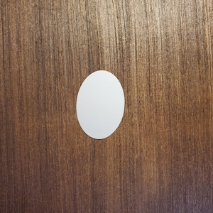 May include: A white oval sticker on a brown wooden surface.