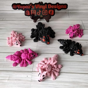 Puede incluir: Seis pequeñas figuritas detalladas pintadas a mano de criaturas con múltiples patas y ojos. Las figuritas son de dos colores: rosa y negro. Las figuritas negras tienen ojos rojos. Las figuritas rosas tienen ojos negros. Las figuritas están dispuestas sobre una superficie de madera clara. @Topaz's Vinyl Designs