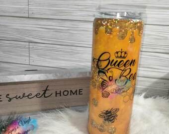 May include: A yellow tumbler with a gold glitter design and a black bee graphic. The tumbler has the text "Queen Bee" with a crown above the word "Queen".