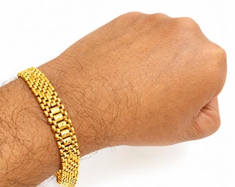 May include: A gold-toned bracelet featuring a dense, multi-row woven mesh link design. The bracelet has a uniform, repeating pattern of small, rectangular metallic links that create a textured, flexible band with a polished, reflective finish.