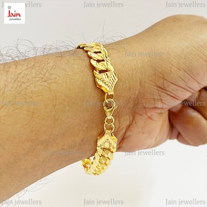 May include: A gold chain bracelet with a textured design. The bracelet is on a person's wrist.