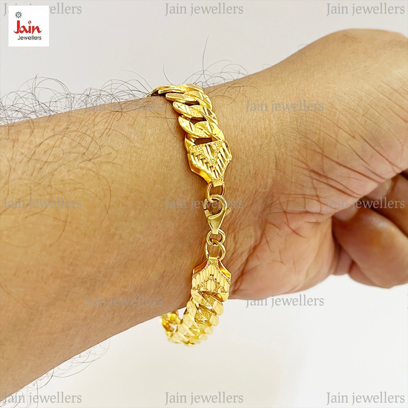 May include: A gold chain bracelet with a textured design. The bracelet is on a person's wrist.