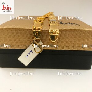May include: A gold chain bracelet with a clasp and a tag that says "WHY". The bracelet is on a gold box with the text "Jain Jewellers" on it.