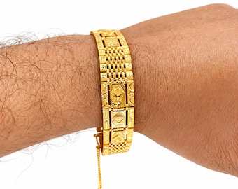 May include: A wide gold bracelet featuring a series of rectangular links with intricate etched patterns and a central mesh-like texture. The bracelet includes a delicate dangling chain attachment at the clasp area, showcasing a polished metallic finish.