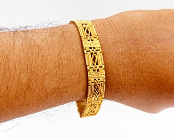 May include: A gold bracelet featuring a series of rectangular links with intricate textured patterns and central openwork details. The metal has a polished finish, and the design consists of repeating segments connected to form a flexible band.