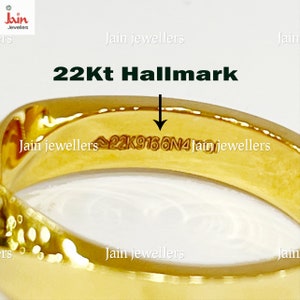 Puede incluir: Primer plano de un anillo de oro con el texto "22Kt Hallmark" y "22K9166N4" grabado en la superficie. El anillo es de color oro brillante y reluciente. La imagen es de una joya.