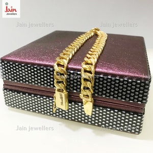 May include: Two gold chains with a curb link design are displayed on a burgundy and black patterned box. The box has the text "Jain Jewellers" printed on it.