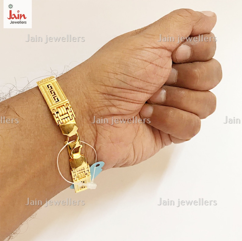 Puede incluir: Un brazalete de oro con un dise&ntilde;o geom&eacute;trico. El brazalete est&aacute; en la mu&ntilde;eca de una persona.