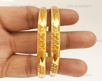 May include: Two gold bangles with intricate designs. The bangles are stacked on top of each other and have a shiny finish.