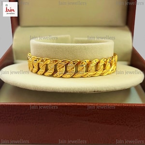 May include: A gold bracelet with a textured, chain-link design. The bracelet is displayed in a red velvet box with the words "Jain Jewellers" printed on the box.
