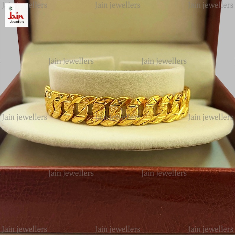 May include: A gold bracelet with a textured, chain-link design. The bracelet is displayed in a red velvet box with the words "Jain Jewellers" printed on the box.