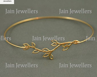 May include: A gold bangle bracelet with a delicate branch and leaf design. The bracelet is open and adjustable.