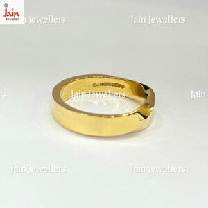 Puede incluir: Un anillo dorado con una banda plana y un dise&ntilde;o ligeramente curvado. El anillo tiene una superficie lisa y pulida y una peque&ntilde;a inscripci&oacute;n en el interior. El anillo es probablemente de oro y es una joya.
