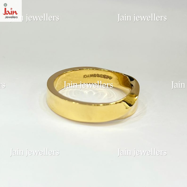 Puede incluir: Un anillo dorado con una banda plana y un dise&ntilde;o ligeramente curvado. El anillo tiene una superficie lisa y pulida y una peque&ntilde;a inscripci&oacute;n en el interior. El anillo es probablemente de oro y es una joya.