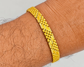 May include: A gold bracelet featuring a multi-link chain design with alternating textured and polished rectangular segments. The bracelet has a repeating pattern of small, interconnected metallic links that create a flexible band structure.