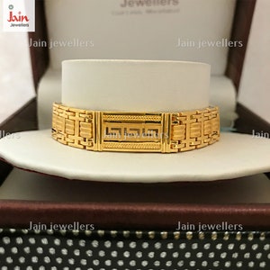 Puede incluir: Un brazalete de oro con un dise&ntilde;o geom&eacute;trico. El brazalete se exhibe en una caja con el texto "Jain Jewellers" impreso en ella.