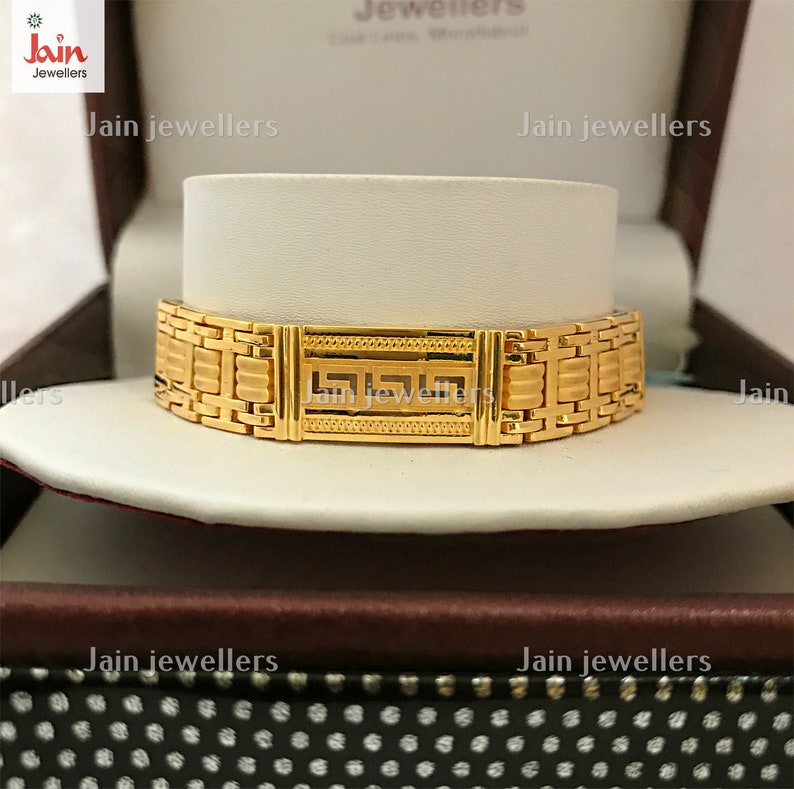 Puede incluir: Un brazalete de oro con un dise&ntilde;o geom&eacute;trico. El brazalete se exhibe en una caja con el texto "Jain Jewellers" impreso en ella.