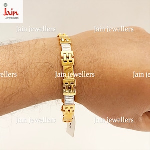May include: A gold and silver bracelet with a square link design. The bracelet is on a person's wrist.