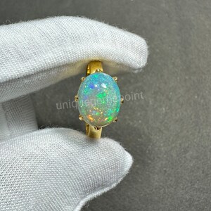 May include: A gold ring with a large oval opal gemstone. The opal has a white base with flashes of green, blue, and red.