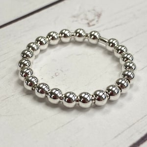 May include: A silver beaded bracelet with a stretchy band. The bracelet is made of round, smooth beads.