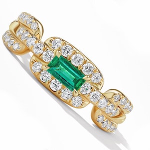 May include: A gold ring featuring a rectangular emerald center stone surrounded by a halo of round diamonds. Additional diamonds are set along the ring's band. The ring is set against a white background.