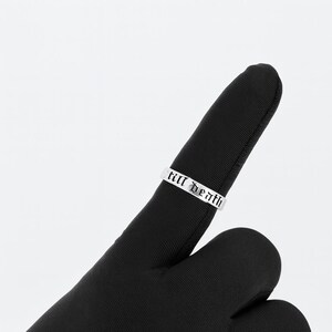 May include: A silver ring with the words "till death" engraved in a gothic font. The ring is displayed on a black surface, creating a contrast that highlights the inscription.