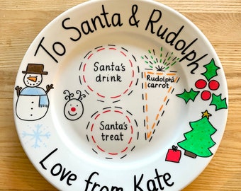 Könnte beinhalten: Ein weißer Keramikt weißer Keramikt weißer Keramikteller mit der Aufschrift To Santa & Rudolph und Love from Kate. Die Illustrationen zeigen einen Schneemann, ein Rentiergesicht, einen Weihnachtsbaum, Stechpalmen, gestrichelte Kreise mit der Beschriftung Santa's drink und Santa's treat sowie eine Karotte mit der Aufschrift Rudolph's carrot.
