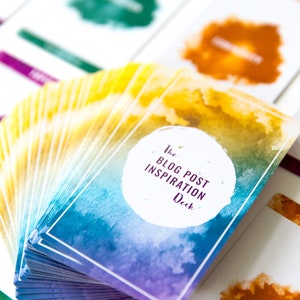 May include: A deck of cards with watercolor designs in shades of blue, yellow, and purple. The cards are labeled "The Blog Post Inspiration Deck".