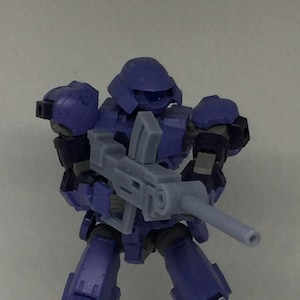 Könnte beinhalten: Eine violett-schwarze, bewegliche Actionfigur eines futuristischen Soldaten, der ein graues Gewehr hält. Die Figur befindet sich in Kampfhaltung, mit Helm und Rüstung. Die Figur ist etwa 15 cm groß.
