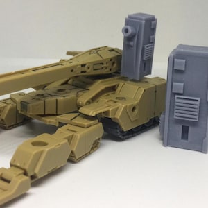 Op de afbeelding: Een beige plastic model van een tank met een lange loop en een grijs plastic accessoire. De tank heeft een gedetailleerd ontwerp met rupsbanden en een torentje. Het accessoire is een rechthoekige doos met een kleine opening aan de bovenkant.