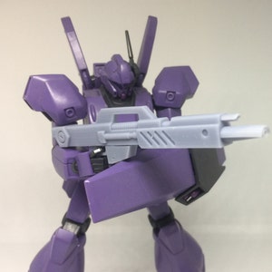 May include: A purple robot holding a gray gun. The robot has a large head with a visor and a large body with a large arm holding the gun.