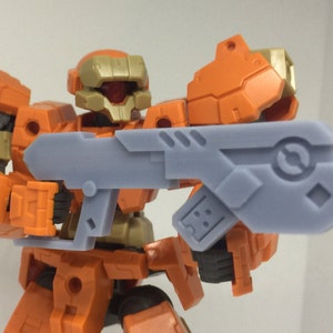 May include: Orange and grey plastic toy robot holding a grey plastic gun. The robot has a gold helmet with a red visor.