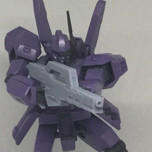 May include: A purple plastic action figure holding a gray plastic gun. The figure has a detailed design and is posed in a dynamic action stance.