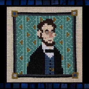 May include: Cross-stitch portrait of Abraham Lincoln in a black suit and blue tie against a green background with gold stars.