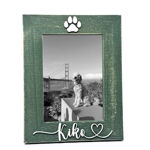 Puede incluir: Un marco de fotos de madera verde desgastada con una foto en blanco y negro de un perro. El marco tiene una huella de pata blanca y el nombre "Kiko" con un corazón recortado. El marco está diseñado para una foto de 13x18 cm.