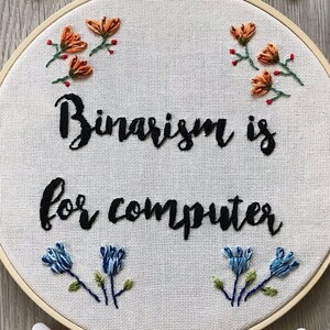 May include: Embroidered hoop art with the text "Binary is for computer" in black cursive font. The hoop is surrounded by colorful embroidery floss spools in blue, orange, and yellow.
