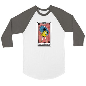 May include: A white and gray baseball tee shirt with a tarot card design. The card is red and pink with a black outline. The card depicts a girl in a yellow dress holding a blue umbrella. The text on the card reads "XIII THE SALTY BITCH".