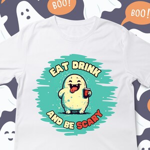 May include: White t-shirt with a green and blue circle graphic featuring a cartoon monster with a red drink and the text "Eat Drink and Be Scary".
