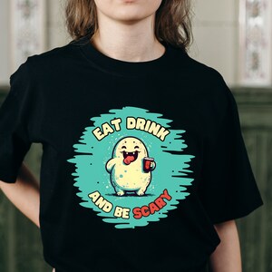 May include: Black t-shirt with a green and blue graphic of a cartoon monster holding a cup. The text on the graphic reads "Eat Drink and Be Scary".