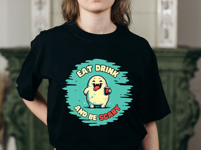 May include: Black t-shirt with a green and blue graphic of a cartoon monster holding a cup. The text on the graphic reads "Eat Drink and Be Scary".
