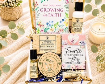 May include: A gift box containing a Mini Devotions Growing in Faith book, a bottle of oatmeal milk honey body lotion, a bar of goat's milk soap, a vanilla lip balm, a body oil roller, and a round candle labeled Be Still & Know Psalms 46:10.