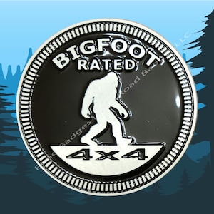 May include: A black and silver round metal pin with a white outline. The pin features a silhouette of Bigfoot walking with the text "BIGFOOT RATED 4X4".