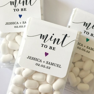 May include: Three clear plastic containers filled with white mints. Each container has a white label with black text that reads "mint to be" and includes the names of a couple and their wedding date. The labels also feature a small heart in a different color.