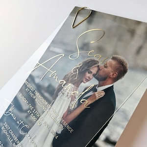 Gold folierte Hochzeitseinladung aus klarem Acryl mit einem Paar Foto im Hintergrund. Sauberes, modernes Design mit Silber, Roségold oder Goldfolie.
