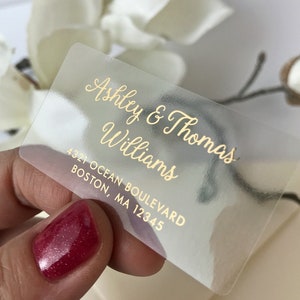 Puede incluir: Pegatina transparente de plástico con letras doradas. La pegatina dice "Ashley & Thomas Williams" y "4321 Ocean Boulevard Boston, MA 12345".