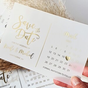 May include: Save the Date card with gold foil lettering for a wedding in March 2024. The card features a calendar with the date circled and a gold heart.