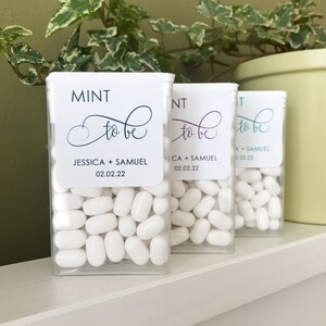 May include: Three clear plastic containers filled with white mints. Each container has a label that reads "MINT to be" with a couple's names and a date. The labels are in navy, purple, and teal.