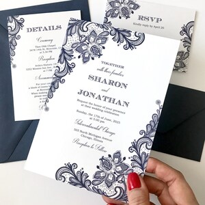 May include: White wedding invitations with navy blue floral lace design. The invitation includes details for the ceremony and reception, with an RSVP card and navy blue envelopes. The invitation reads "Sharon and Jonathan" and the date of the wedding.