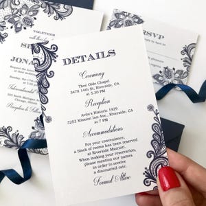 Puede incluir: Elegante juego de invitaciones de boda con diseño de encaje floral azul marino sobre cartulina blanca. Incluye invitación, tarjeta de confirmación y tarjetas de detalles. Una cinta y un sobre azul marino completan el conjunto. La invitación detalla la ceremonia, la recepción y el alojamiento.