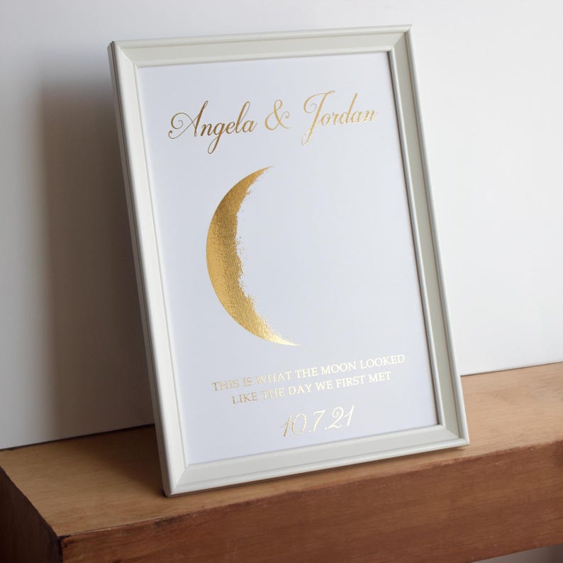 May include: White framed print with gold text and a gold crescent moon design. The text reads "Angela & Jordan", "This is what the moon looked like the day we first met", and the date 10.7.21.